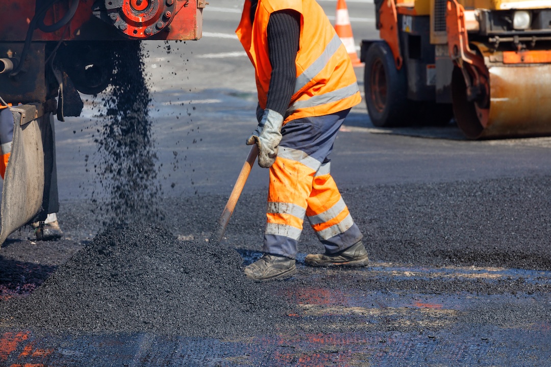 Crew member shoveling hot mix asphalt