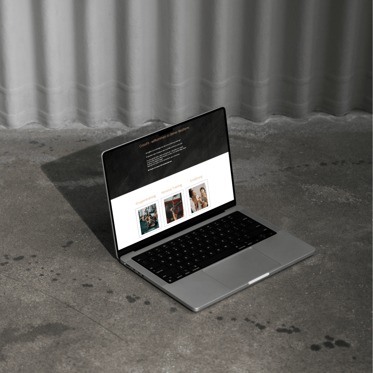 Laptop auf grauem Steinboden vor grauer, geriffelter Wand. Ein Bild einer Website ist auf dem Bildschirm zu sehen.
