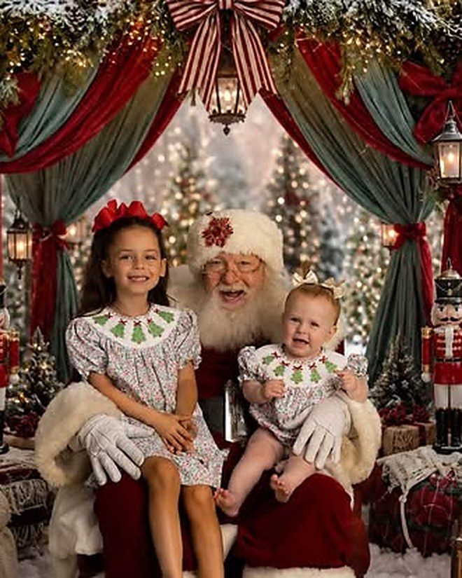 Two sisters in matching Christmas dresses sitting with Santa under the garland arch