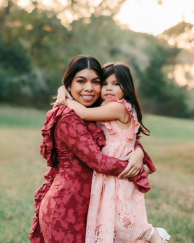 A mother and her daughter laughing together in a field at sunset