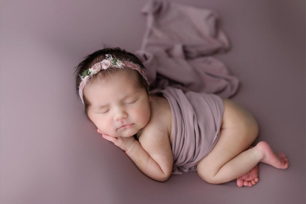 Newborn baby girl asleep in a mauve wrap