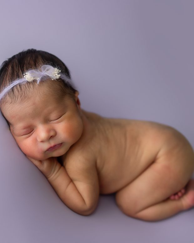 Newborn baby girl asleep on a lavender backdrop