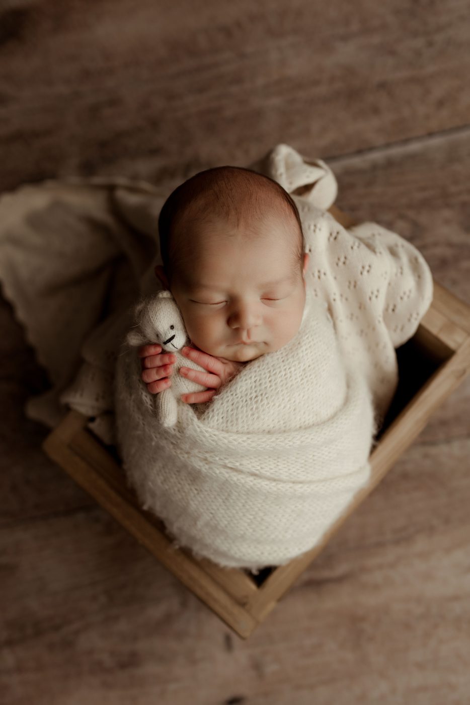 Newborn swaddled in cream in a small wooden bed
