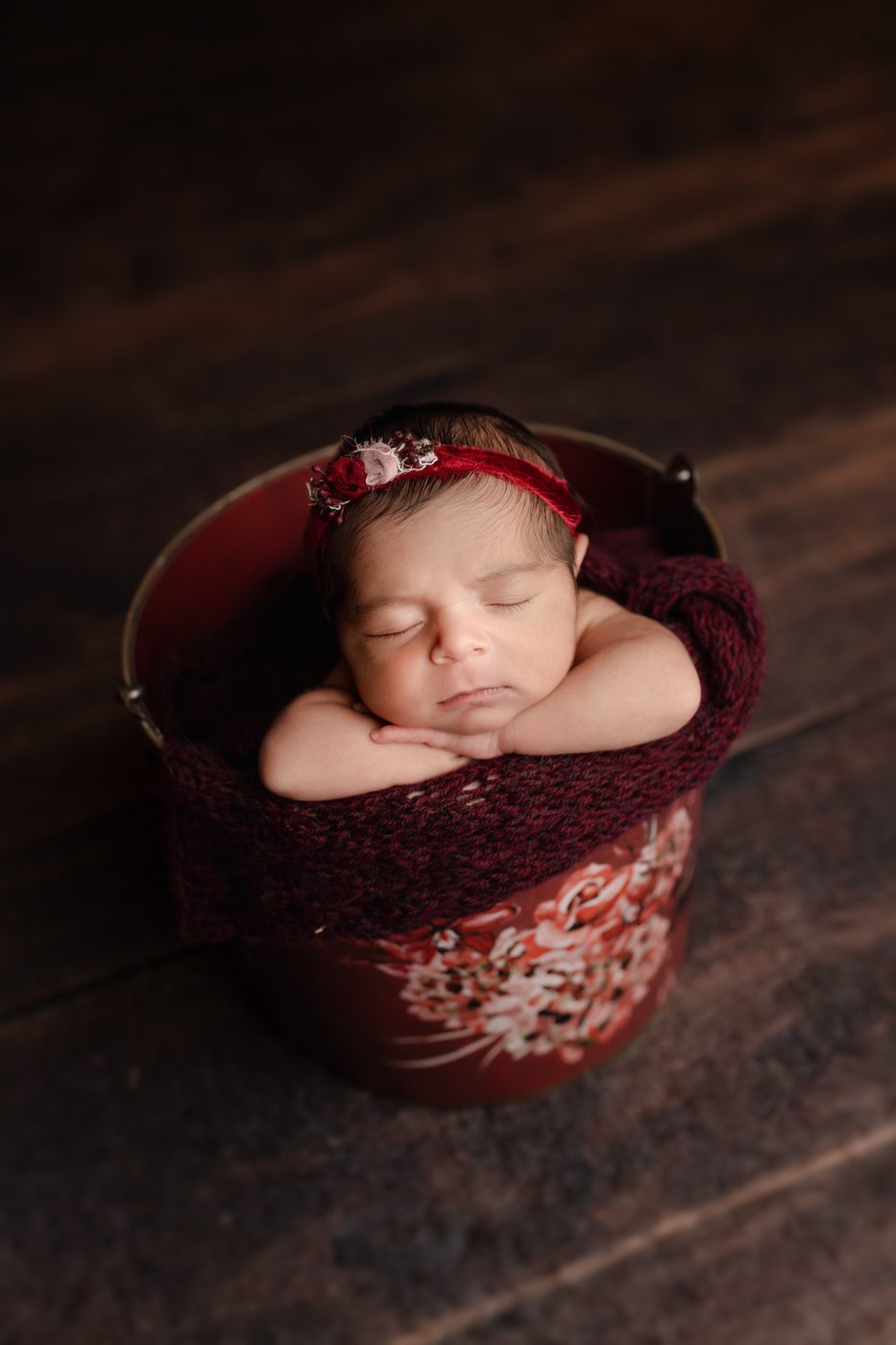 Newborn girl curled in a dusty-rose bucket
