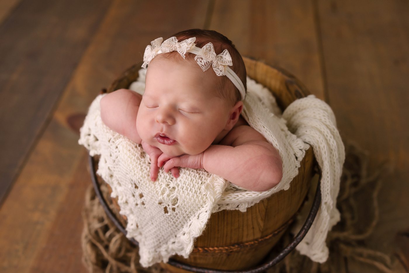 Newborn asleep in a wooden barrel with lace trim