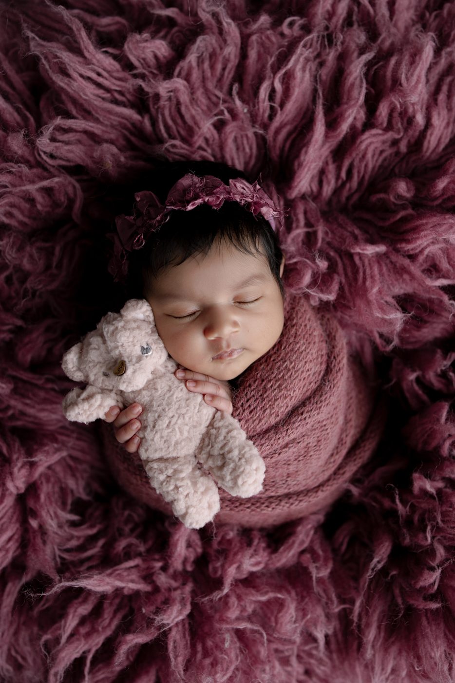 Newborn girl with a tiny teddy on a plum flokati