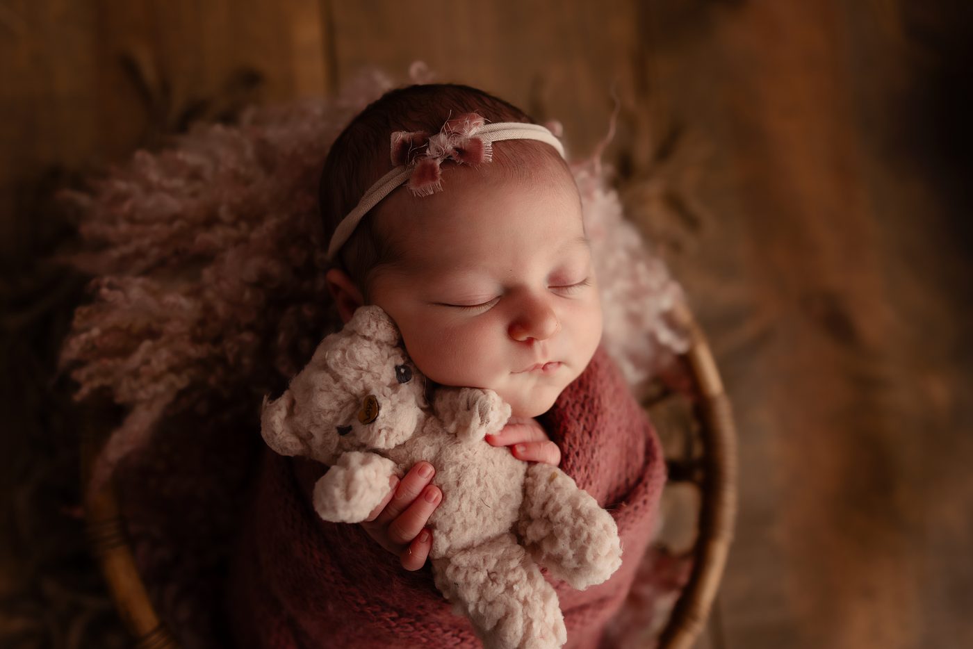 Newborn girl with a teddy bear in a warm brown bowl