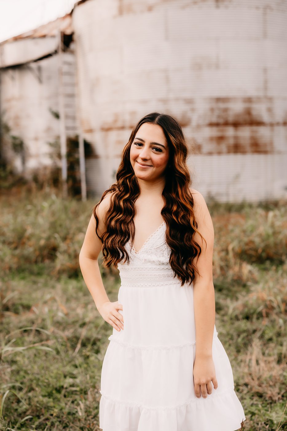 Senior girl in a white dress beside a weathered barn