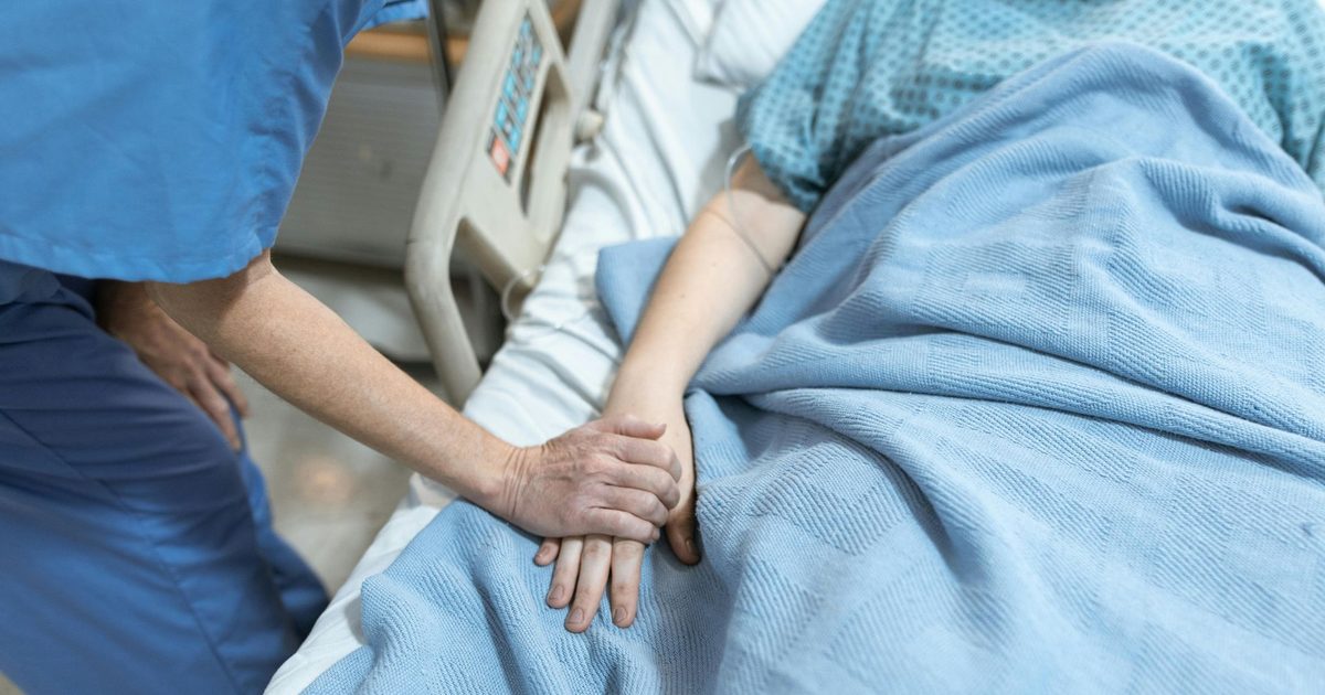 A nurse in scrubs holding a patient's hand