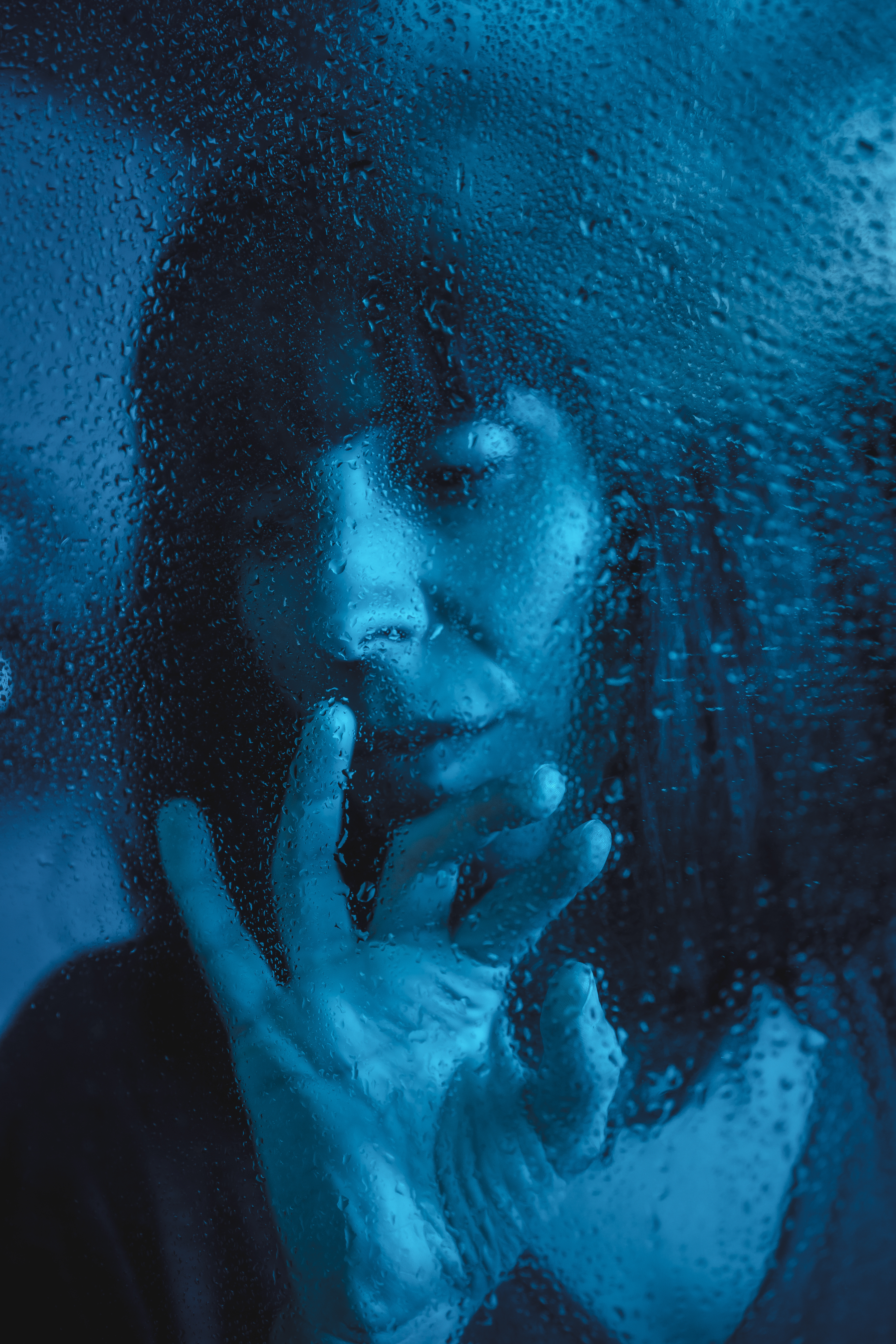 Person looking out of a rainy window in quiet introspection representing the blue world nervous system shutdown and withdrawal