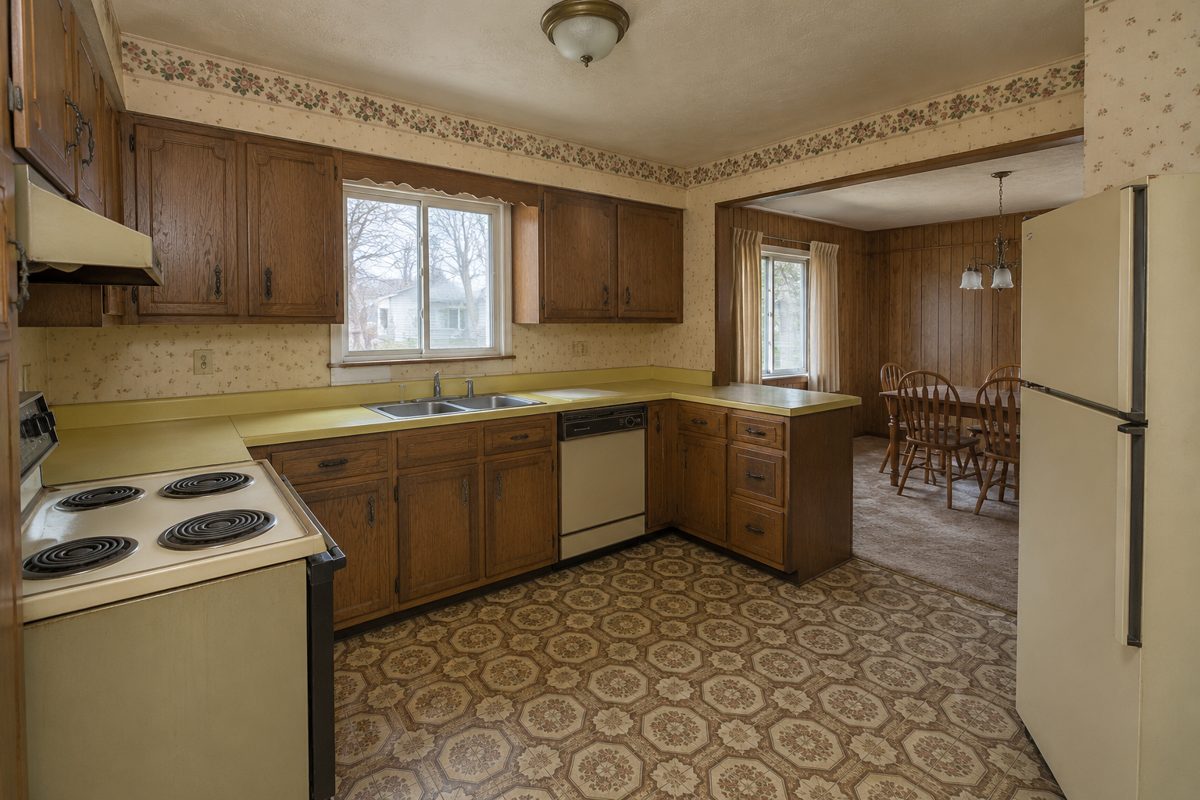 Dated kitchen with worn wood cabinets, yellow countertops and patterned vinyl flooring