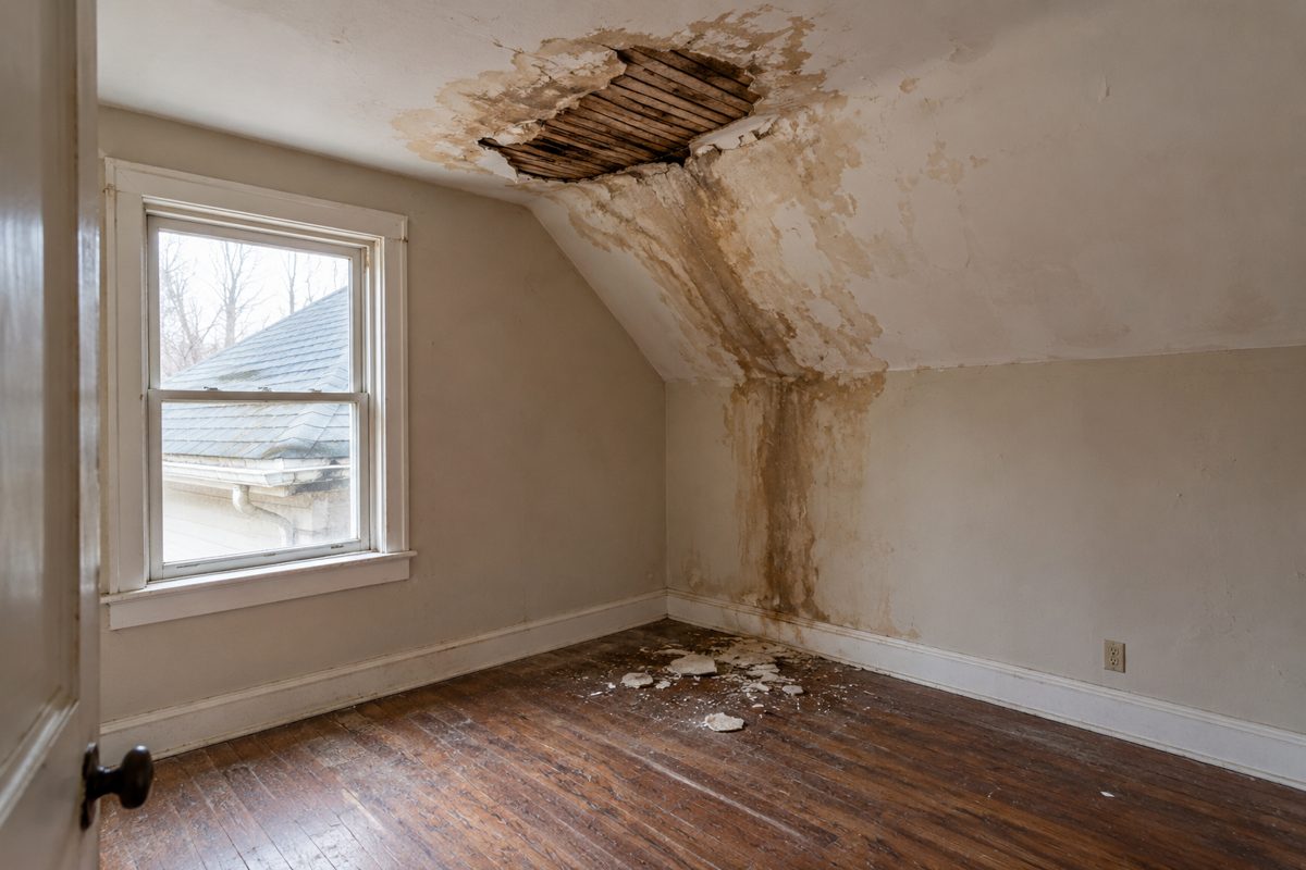 Bedroom with brown ceiling and wall stains and missing plaster from a roof leak