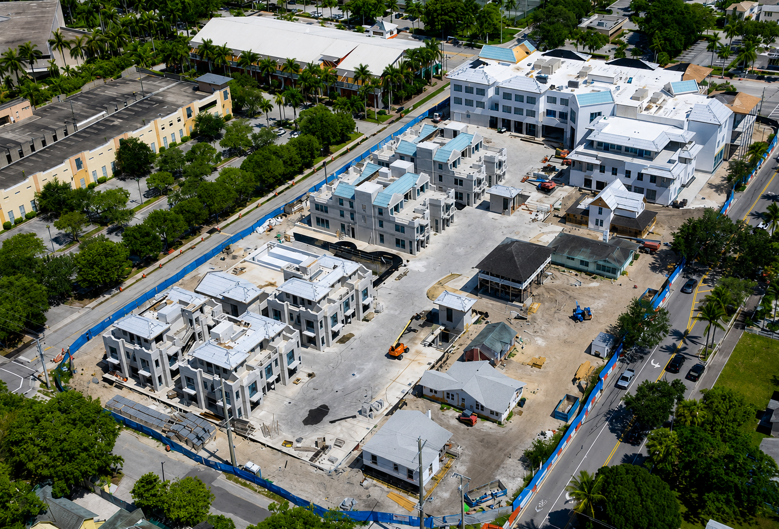 Aerial view of a condominium construction site with multiple low-rise buildings and blue perimeter fencing.