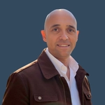 Professional man smiling in a brown jacket, representing career coaching services for clarity and confidence in job progression.