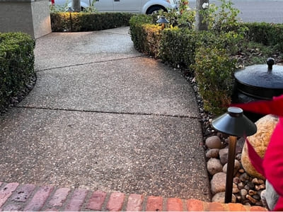 Pathway lighting along a curved residential walkway, bordered by hedges and stones, providing safe evening access.