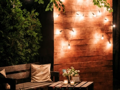 Outdoor patio area with string lights on a wooden wall, creating a cozy and inviting ambiance in a garden seating space.