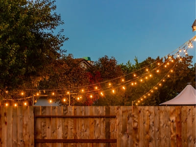 String lights hanging above a wooden fence in a backyard, creating a warm and festive atmosphere at dusk