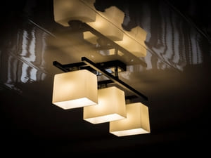 Modern ceiling light fixture with three square-shaped lights, casting a warm glow in an indoor space.