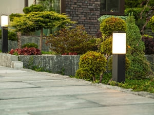 Garden pathway illuminated by square post lights, accentuating the well-manicured landscaping and stone walkway.