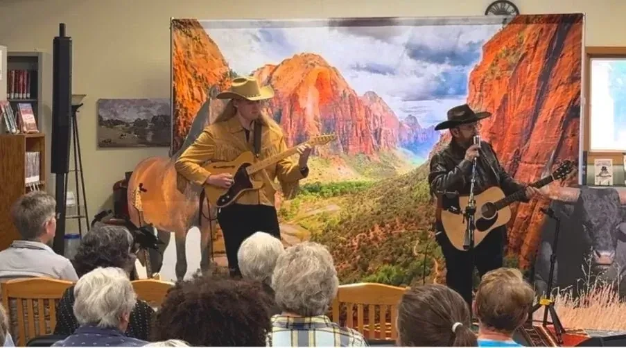Ethan Elseth and Terry Derosier performing for a seated audience with their Western backdrop and stage props