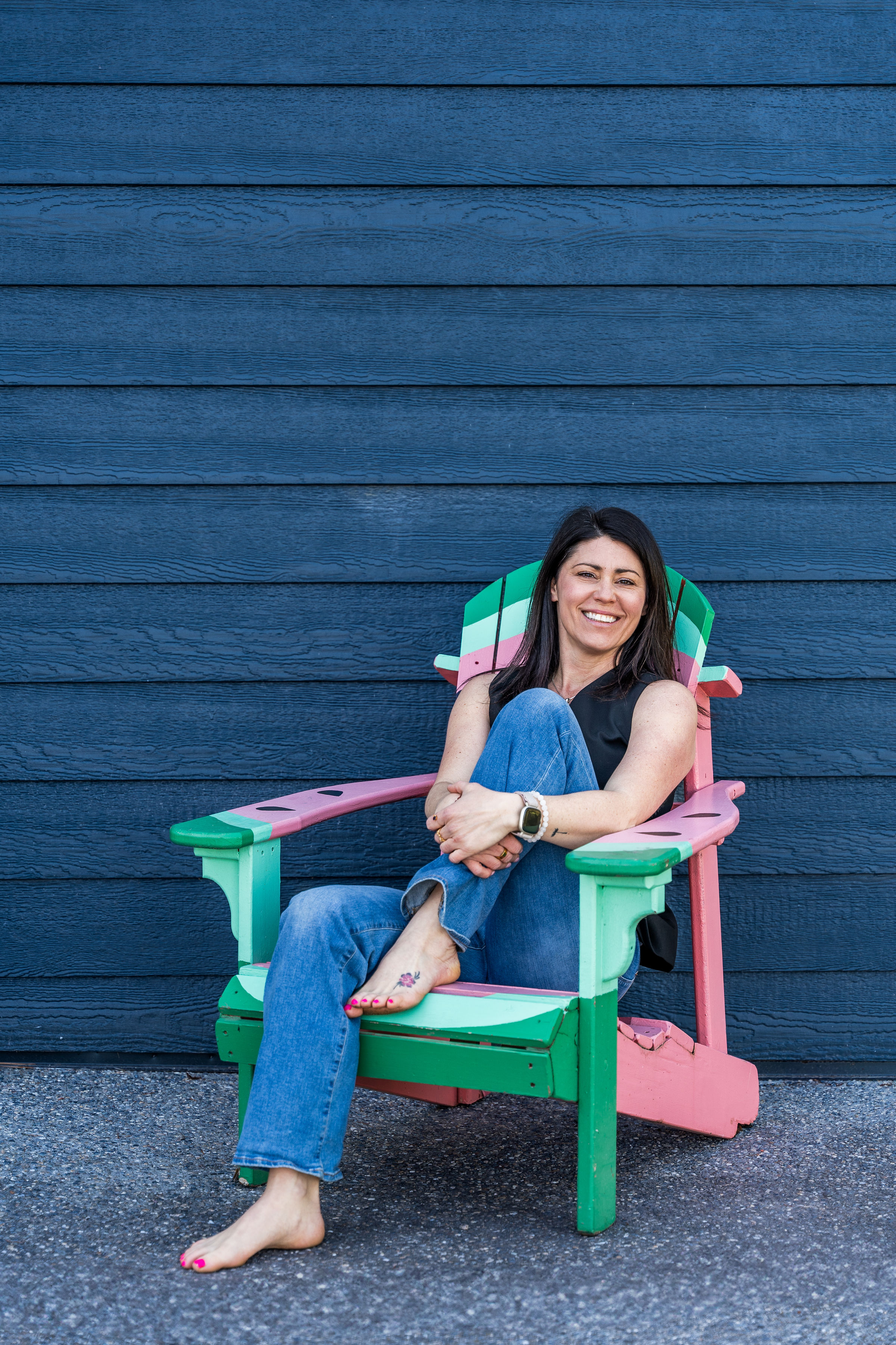 Woman sitting in a colorful Adirondack chair against a blue wooden wall, representing Andrea Nicole Design's focus on intentional living and exterior color consultation.