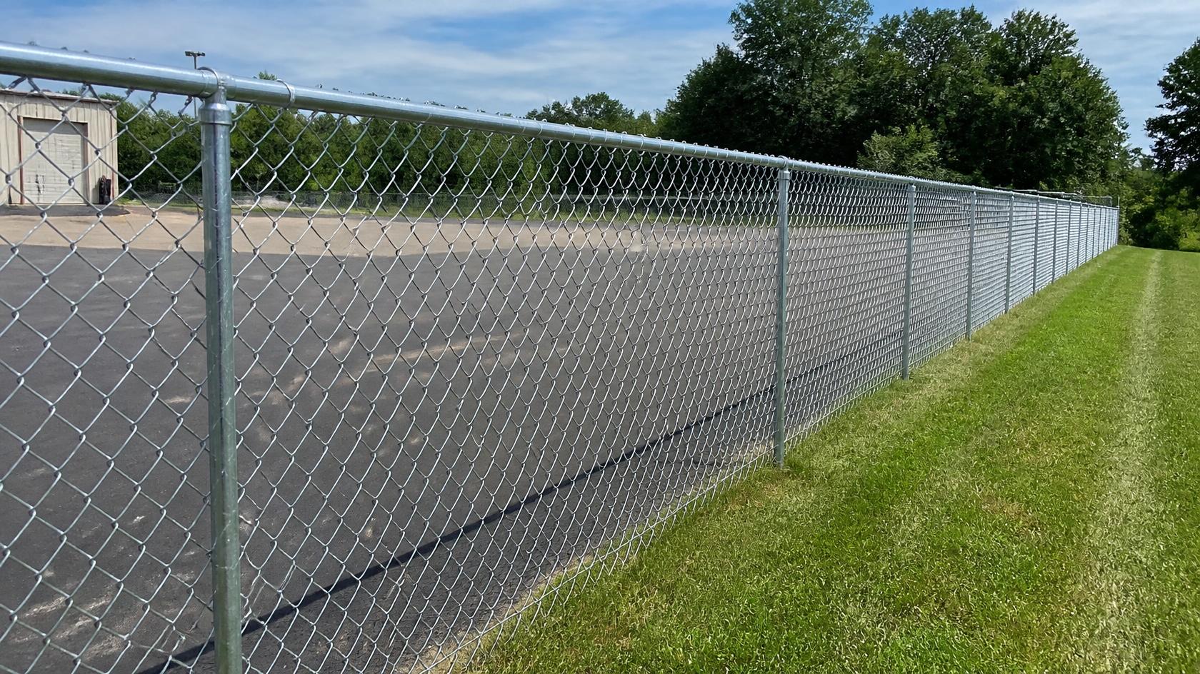 Contractor evaluating a worn commercial chain link fence in Oregon, IL with damaged mesh, leaning posts, and deteriorated sections that may need replacement.
