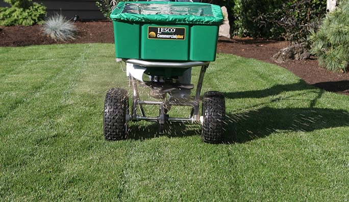 Technician applying fertilizer with a spreader on a Seattle lawn