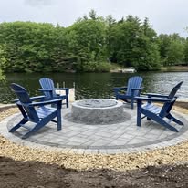 Lakefront fire pit with blue Adirondack chairs by American Landscape Construction