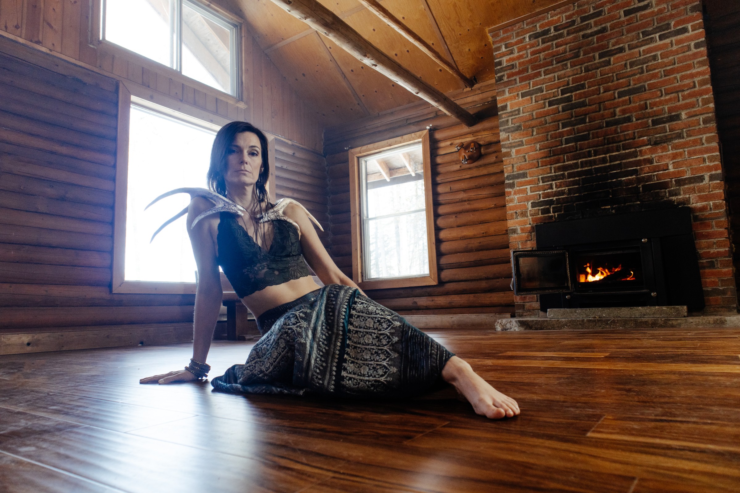 Seated on the cabin floor by the fire, antler across the shoulders