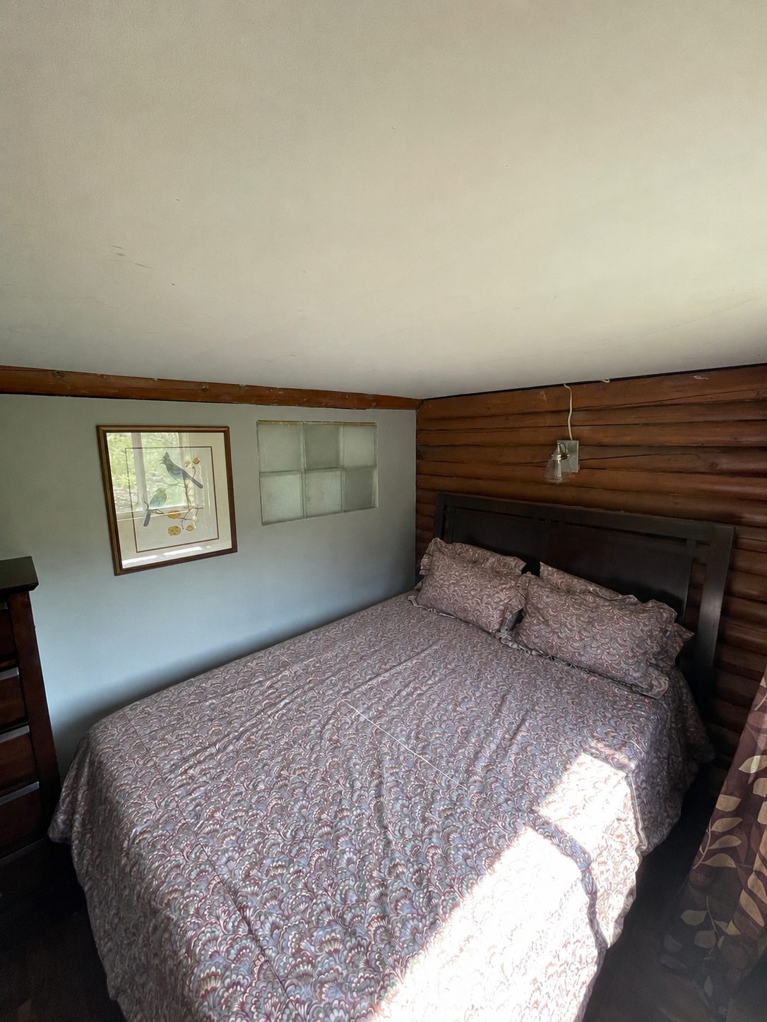 The second bedroom—a queen bed against the log wall beneath a glass-block window