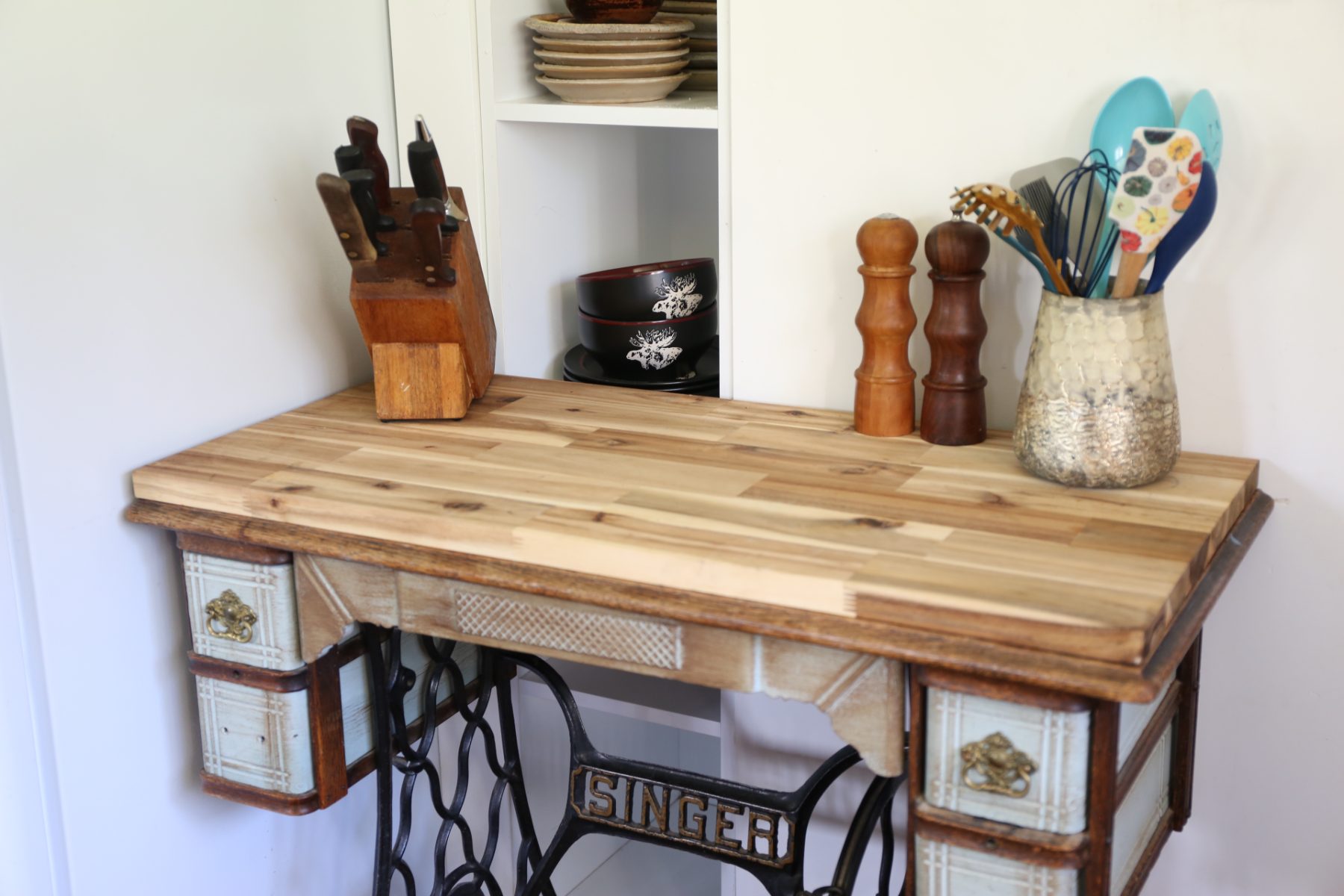 A butcher-block top on an antique Singer treadle base, with knives, mills and stoneware