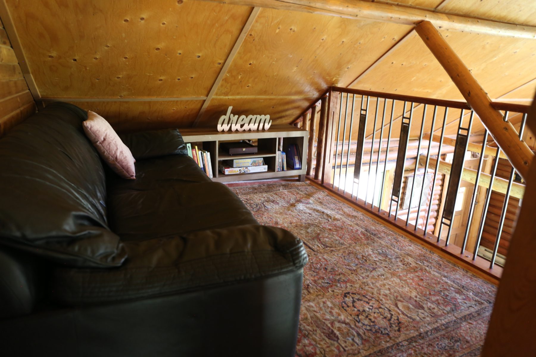 The loft sitting area—leather sofa, shelf of books and board games, opening over the great room