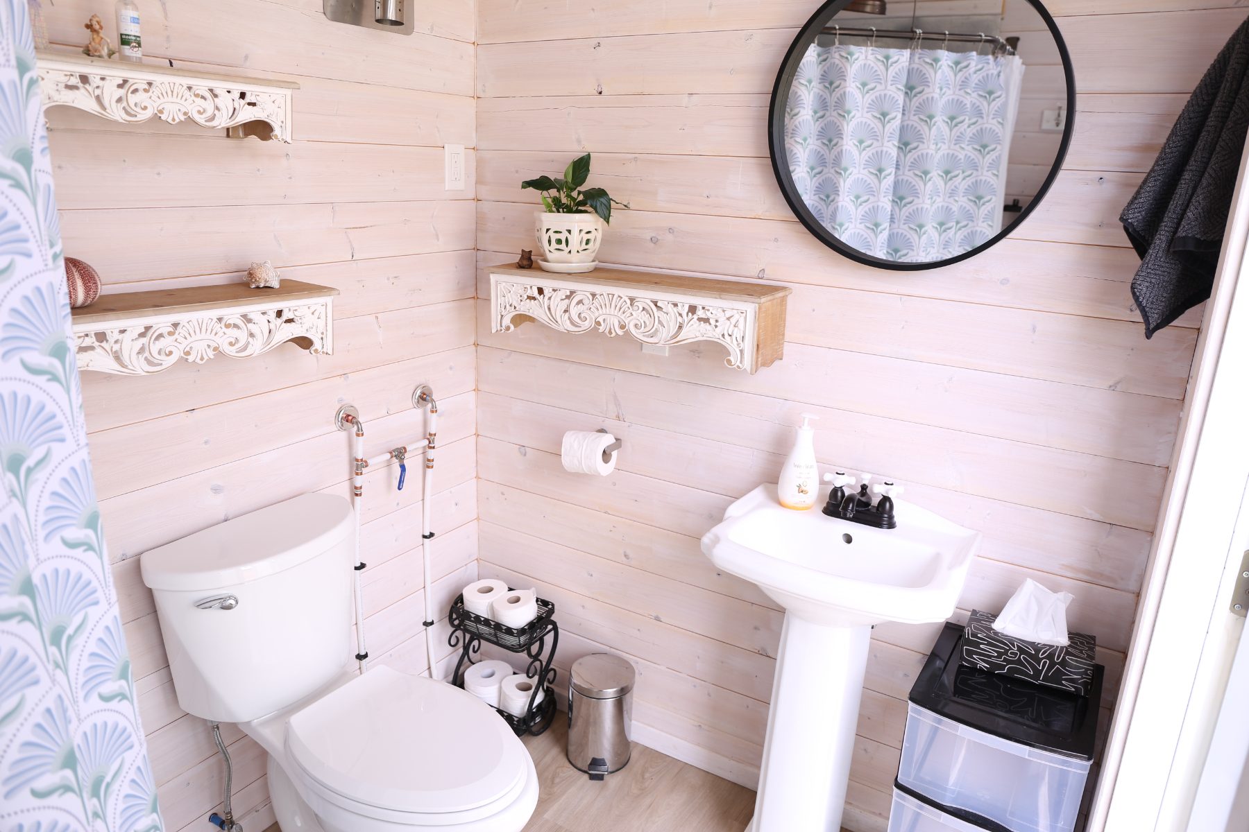 Inside the washhouse—pedestal sink, round mirror, shower and shiplap walls
