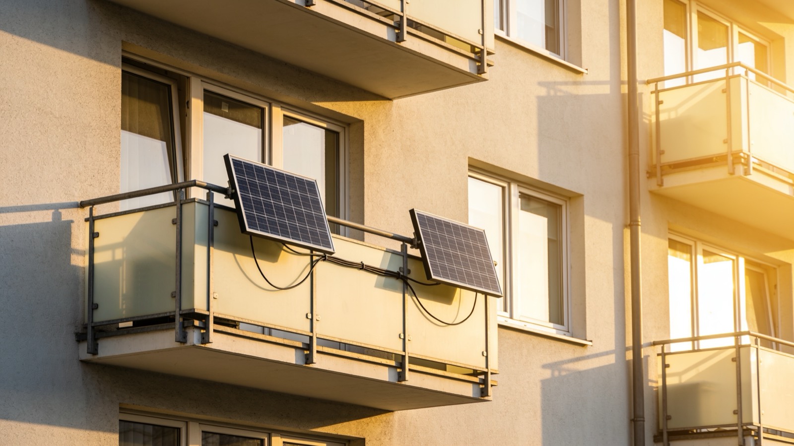 Zwei Solarmodule an einem Balkongeländer eines Mehrfamilienhauses fangen die Morgensonne ein und speisen über einen kleinen Wechselrichter Strom ins Hausnetz
