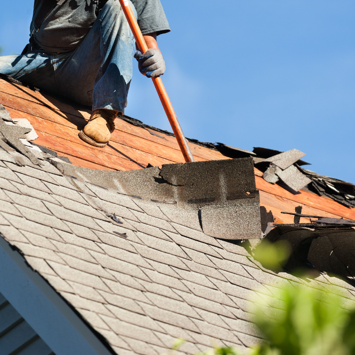 Worker repairing a roof, removing damaged shingles, showcasing the importance of roof maintenance and inspections for residential properties.