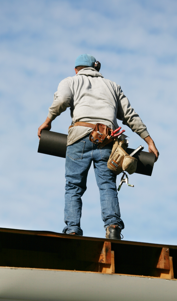 Roofer standing on a commercial building rooftop, holding roofing material, emphasizing maintenance and installation of durable roofing solutions.