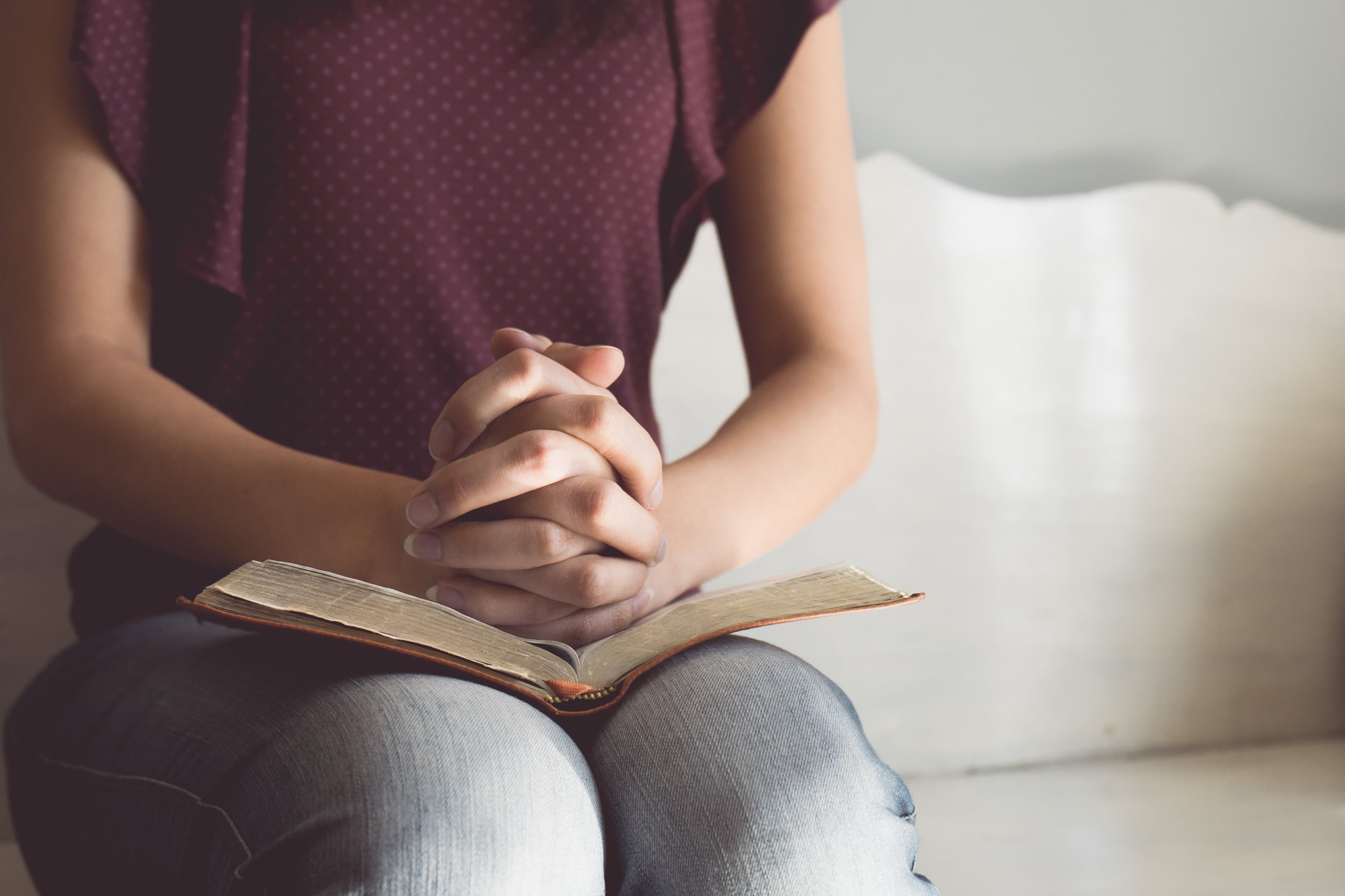 Hands folded in prayer over an open Bible