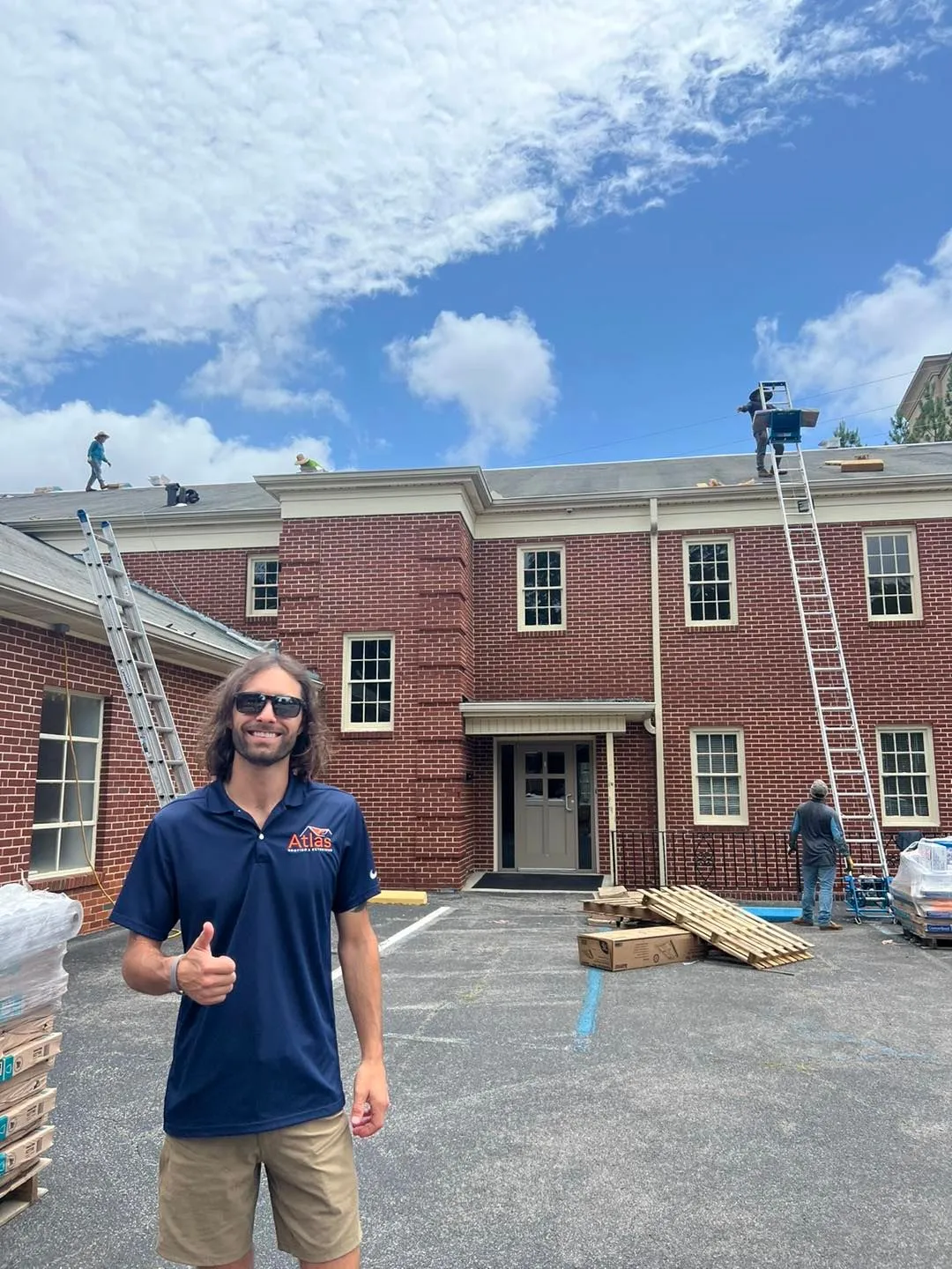 Team member giving a thumbs up in front of a brick building with roofers working above