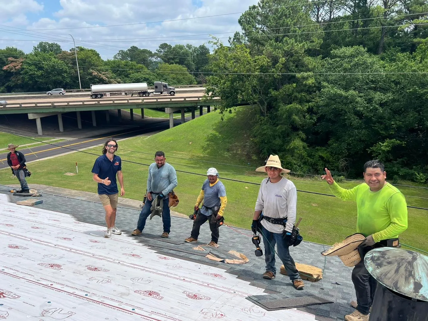 Roofing crew standing on a sloped roof beside a highway overpass