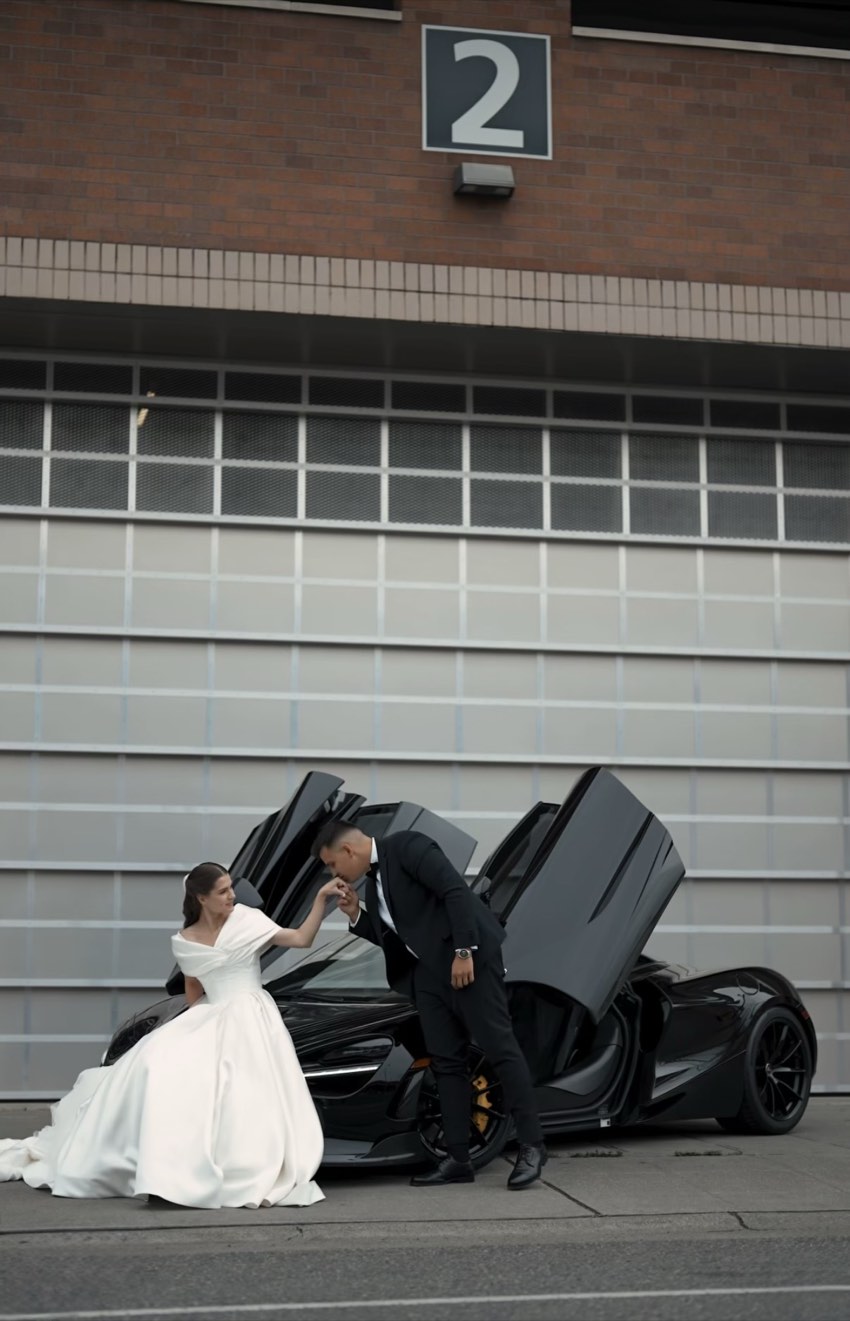 Groom kissing the bride's hand beside a black McLaren 720S