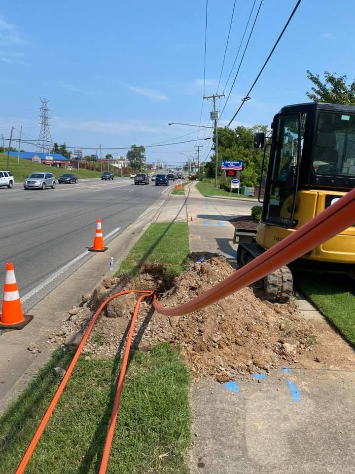Roadside underground utility conduit trenching with excavator and orange conduit