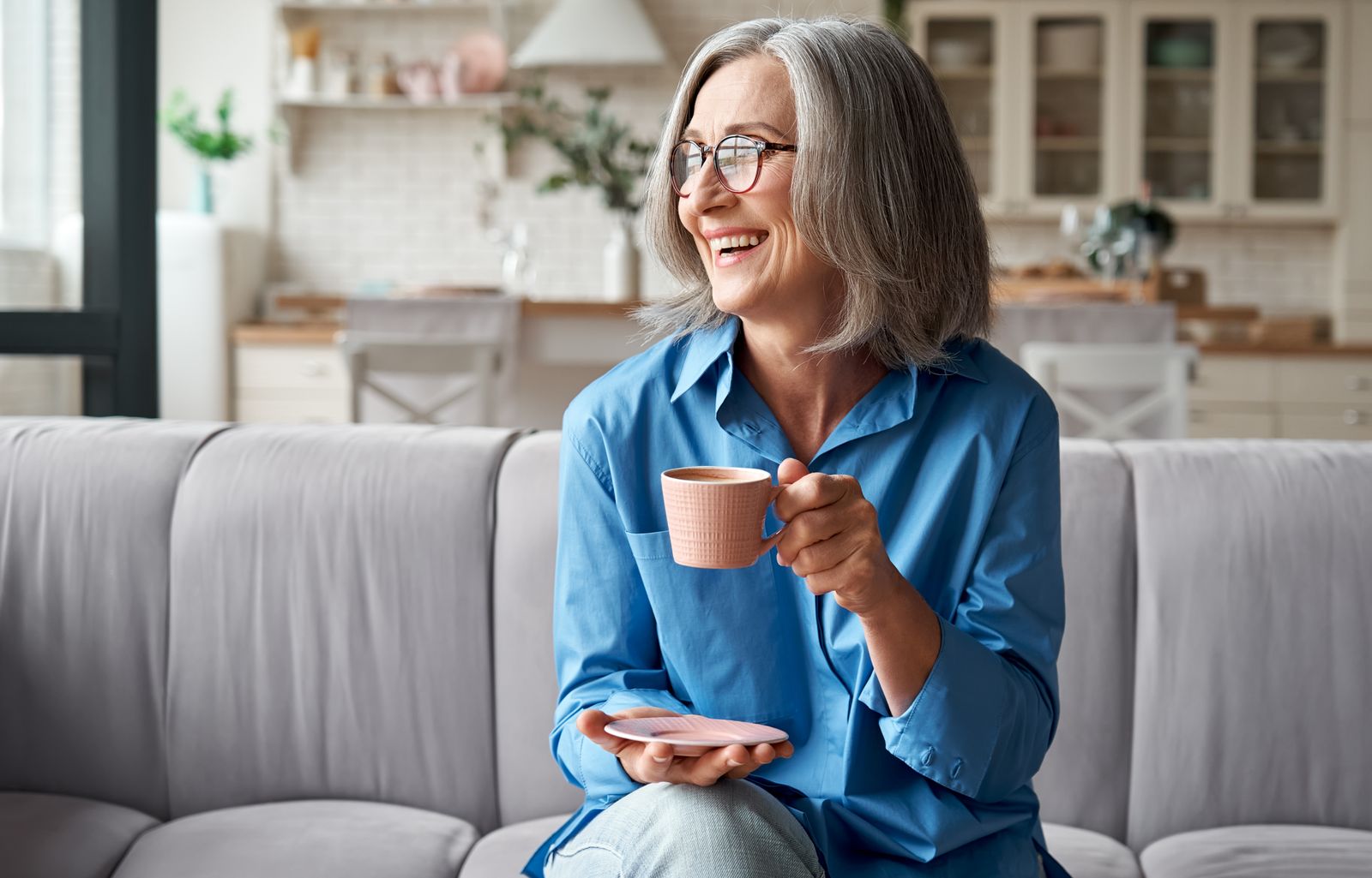 Smiling older woman relaxing on a sofa with a cup of coffee