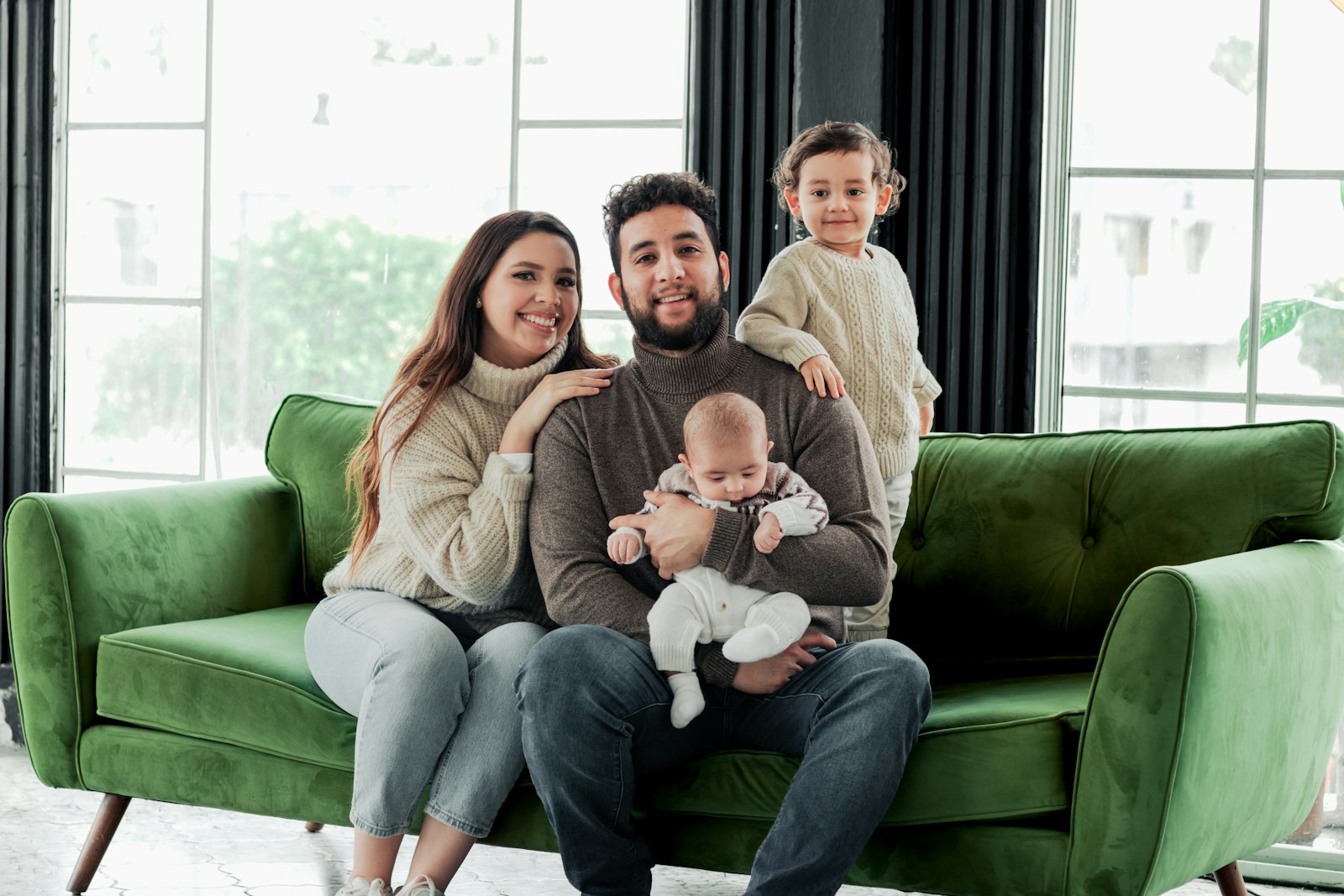 Young family with two small children smiling on a green couch at home