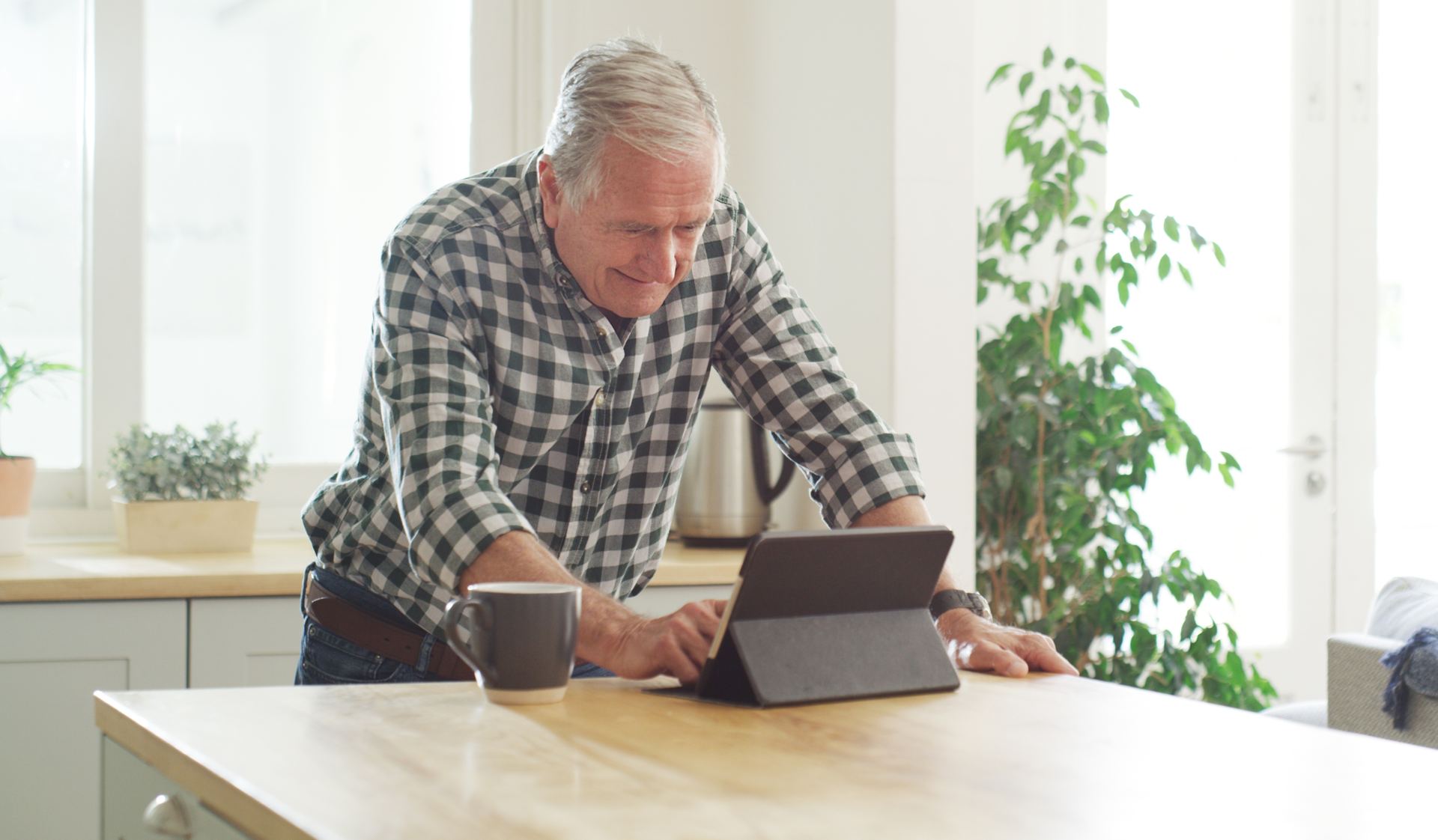 Older man reviewing options on a tablet at his kitchen table