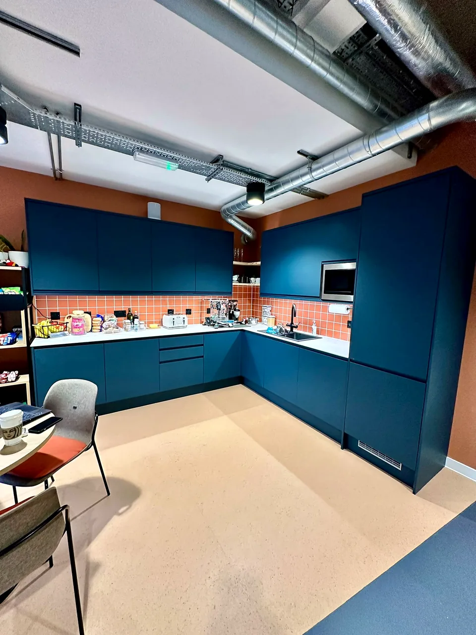 The tea point at Kaluza, with deep blue cabinetry set against exposed brickwork.