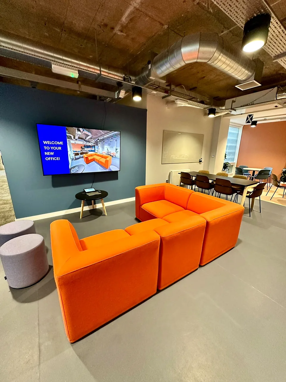 Modular orange breakout seating beneath exposed concrete and services in the Kaluza office.