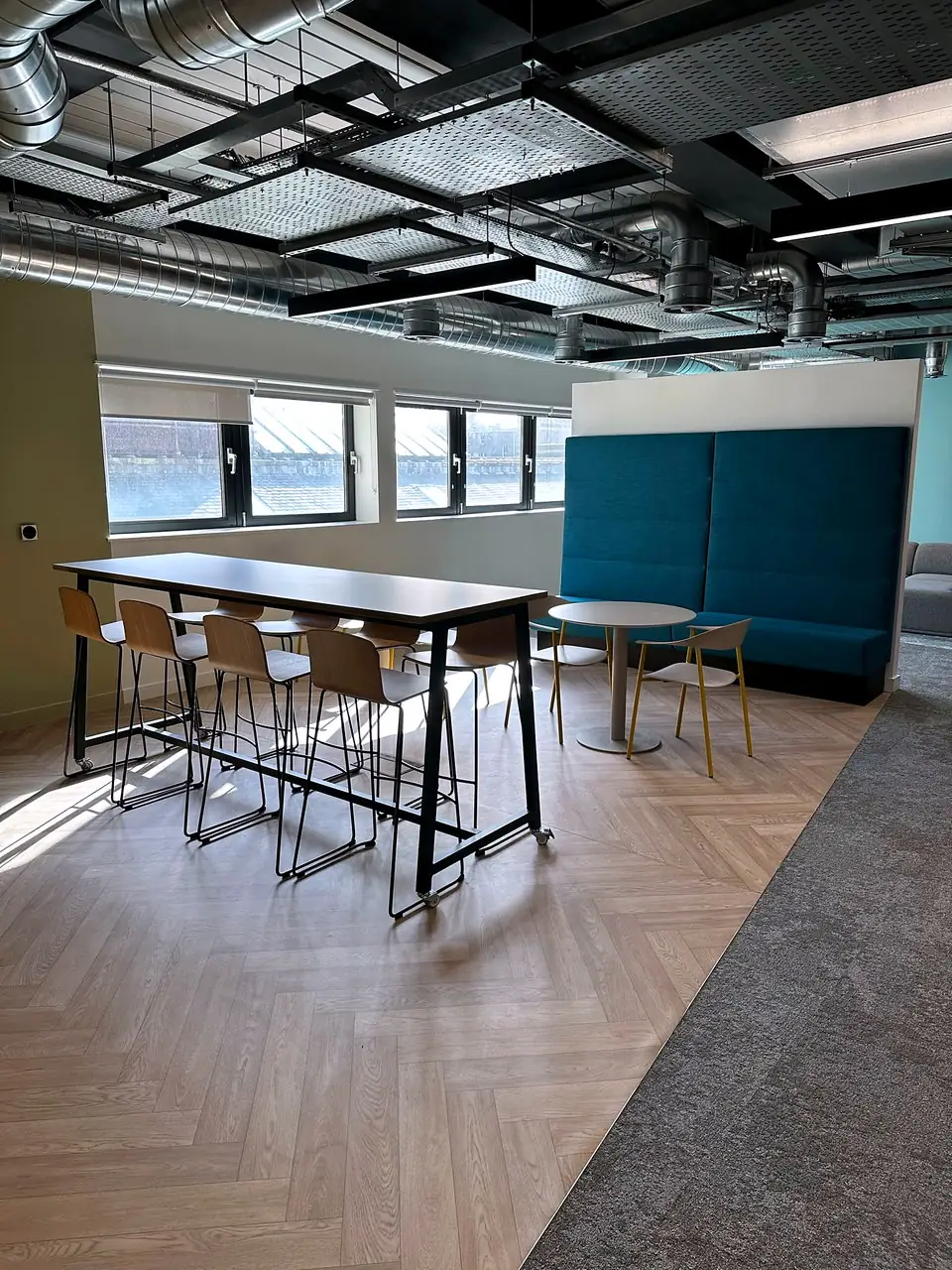 High tables and stools beside a teal acoustic booth in the breakout area at 33 Castle Street.