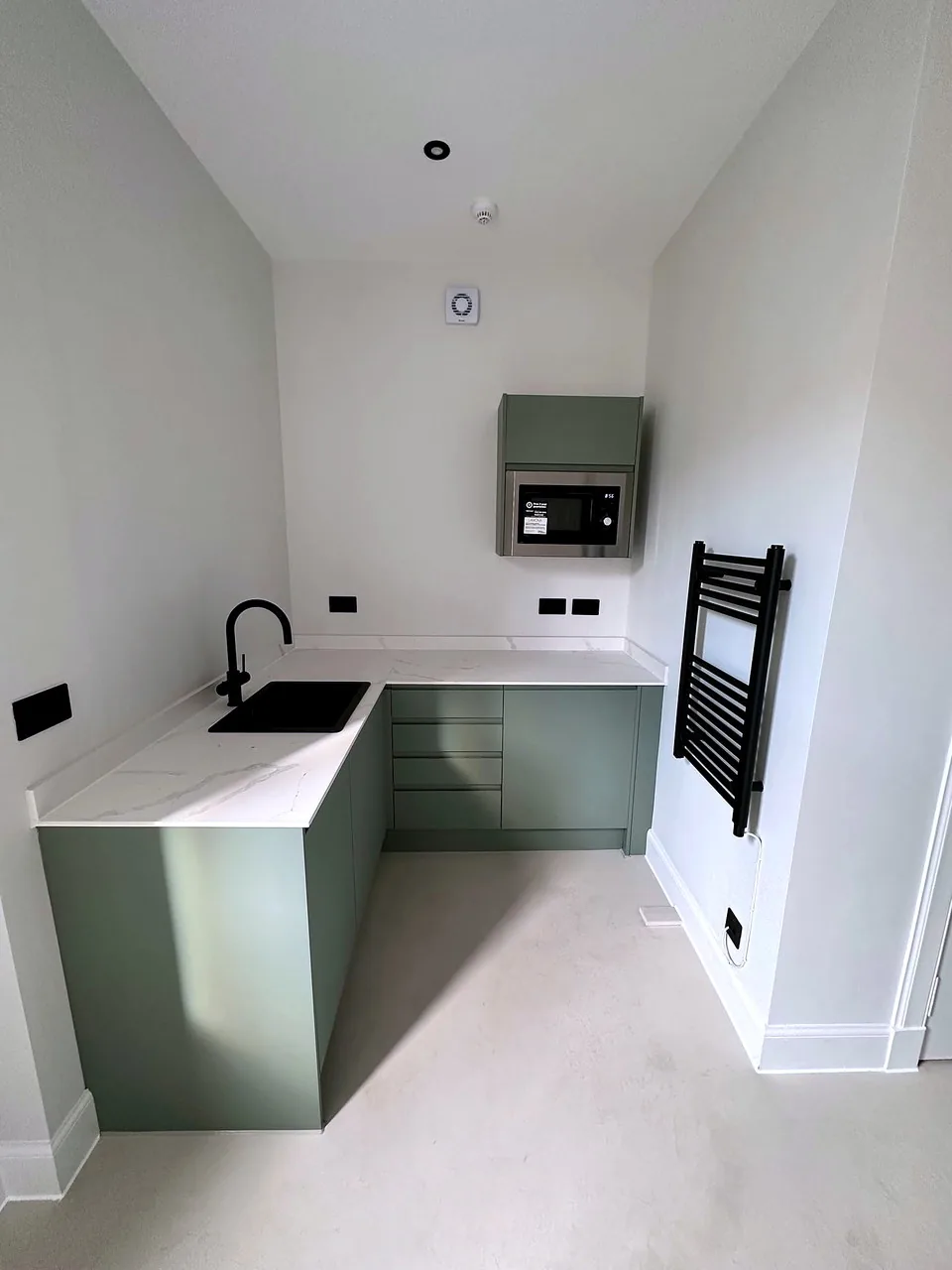 A compact kitchen with sage green cabinetry and a black tap at Broughton Street Lane.
