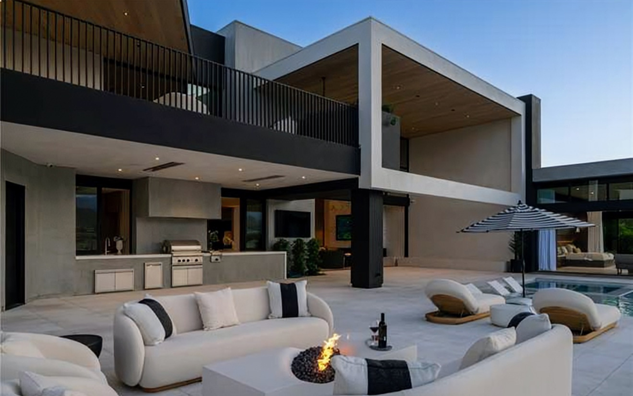 Covered patio lounge with outdoor kitchen, fire table and curved sofas beside the pool