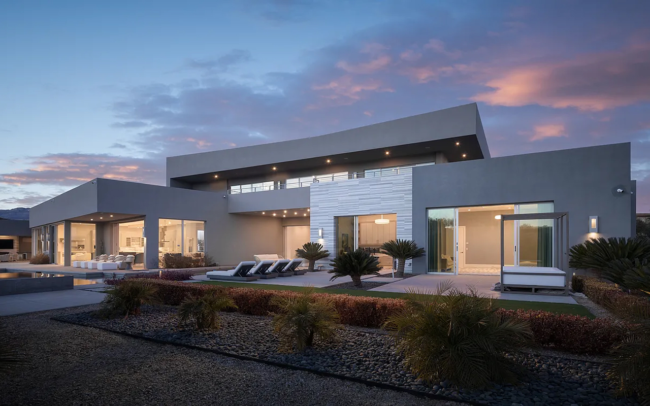 Desert modern estate at sunset with sculpted rooflines and poolside chaise lounges